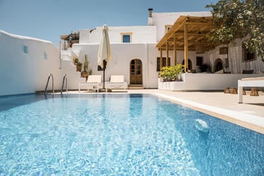 Luxury Greek villa with a sparkling blue infinity pool and sun loungers under a white Cycladic house.