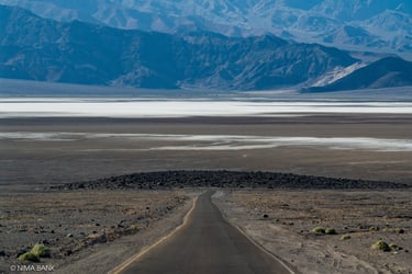a hazy expanse of mountains intersected by a windy dirt road & salt basin in death valley california
