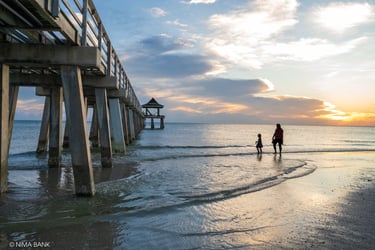 mother and child walking in the gulf of mexico with shimmering waves by the naples pier