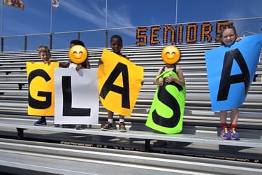young kids holding signs that spell out GLASA and standing on bleachers