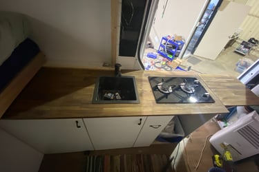 Custom camper van kitchen with wood countertop, black sink, and two-burner gas stove.