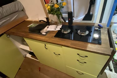 Camper van kitchen featuring a wooden countertop with a two-burner gas stove and yellow cabinets.