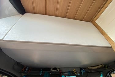 Custom white overhead storage cabinet inside a camper van with a wood paneled ceiling and storage line.
