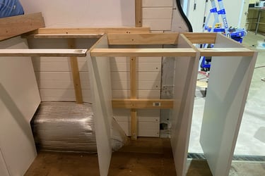 Custom wooden kitchen cabinet frames being installed during a DIY van conversion project.