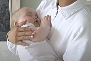 A white baby being rocked and held to the chest of a Filipino woman.