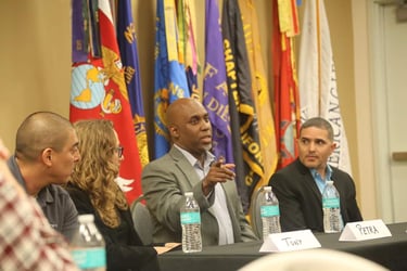 Lee Jones in a suit and tie is sitting at a table with a microphone