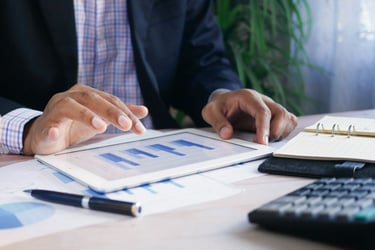 Hands of person of color at a desk looking at bar graphs on a tablet