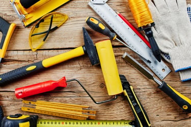 Collection of construction hand tools including a hammer, saw, and ruler on a wooden workbench.