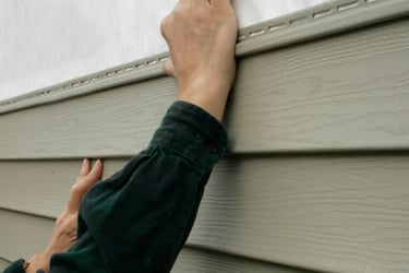 A contractor installs vinyl siding panels on a residential home exterior.