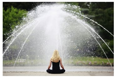 Une femme assise devant une fontaine en position de méditation.