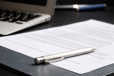 A silver ballpoint pen resting on a signed legal document or contract next to a laptop computer on a desk.