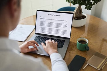 Copywriter typing a history homework assignment on a laptop at a wooden desk with coffee.