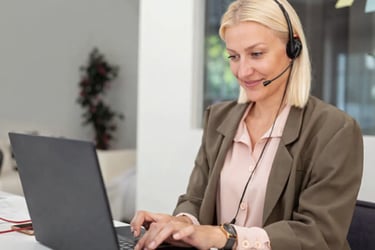 A professional blonde female customer support representative wearing a headset and working on a laptop.
