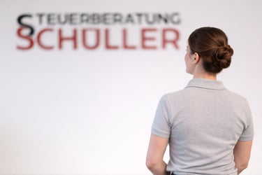 Mit dem Rücken zugewande Frau, im Hintergrund Schriftzug Steuerberatung Schüller