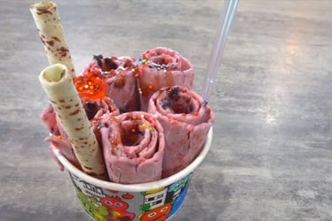 Handmade strawberry rolled ice cream in a cup with sprinkles and wafer rolls.