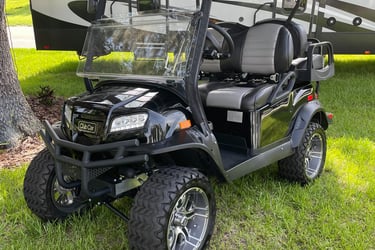 Custom black Club Car golf cart with off-road tires and lift kit parked on grass.