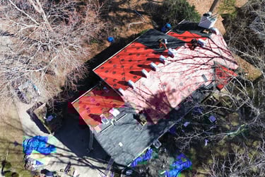Aerial view of contractors installing new roof shingles over red underlayment on a residential home.