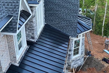 A high-angle view of a residential roof featuring a mix of black standing seam metal and architectural shingles.