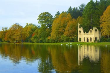 Autumn foliage and stone ruins reflecting in a calm lake at Painshill Park landscape garden.