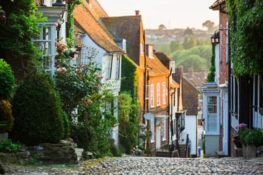 Quaint cobblestone street in Rye, England, with historic timber-framed houses and ivy at sunset.