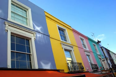 Brightly colored pastel houses along Portobello Road in Notting Hill, London, under a clear blue sky.