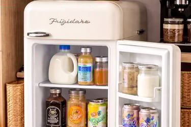 Open Frigidaire retro mini fridge stocked with beverages and milk in a home coffee station.