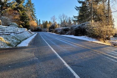 a road with snow on both sides with a white fence and bushes