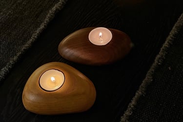 Two lighted tea light candles in smooth, pebble-shaped wooden holders on a dark surface.