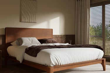 Modern wooden bed frame with white bedding in a minimalist bedroom with soft natural lighting.