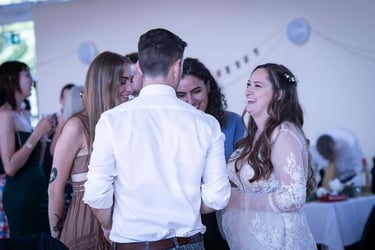 A laughing bride in a lace wedding dress talks to guests during an indoor reception.