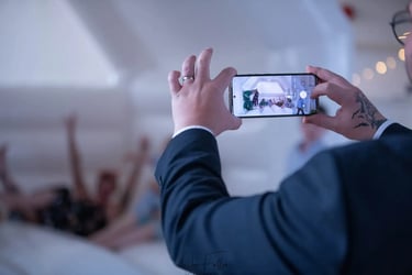 A wedding guest takes a smartphone photo of friends posing inside a white inflatable bouncy castle.