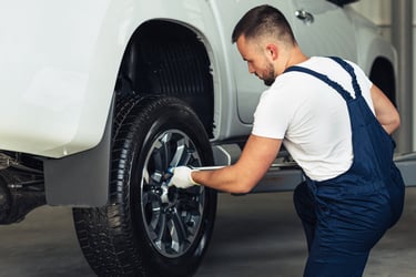 Professional mechanic changing a car tire on a white pickup truck in an auto repair shop.