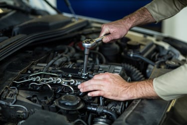Professional auto mechanic using a socket wrench to perform engine repair and maintenance services on a vehicle.