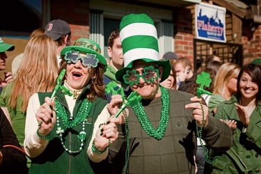 People celebrating St. Patrick's Day wearing green hats, shamrock glasses, and beads at a festive parade.