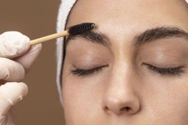 Técnica profesional de cejas aplicando gel de laminado en las cejas de una mujer con un cepillo