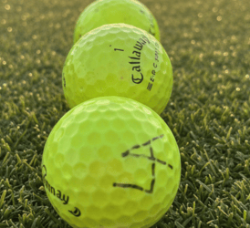 Three yellow Callaway golf balls lined up on a green grass fairway at sunset.