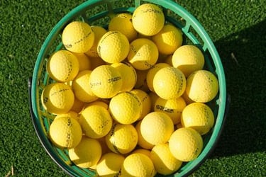 A green plastic basket filled with yellow golf balls on a synthetic grass practice green.