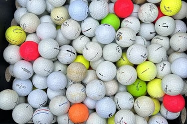 A black plastic crate overflowing with assorted used golf balls from brands like Callaway, Titleist, and Srixon.
