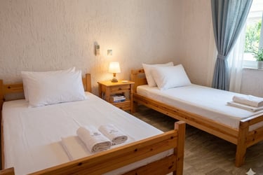 Two single wooden beds with white linens and rolled towels in a bright guest bedroom.