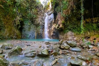 Scenic forest waterfall cascading into a turquoise pool surrounded by mossy rocks and lush greenery.