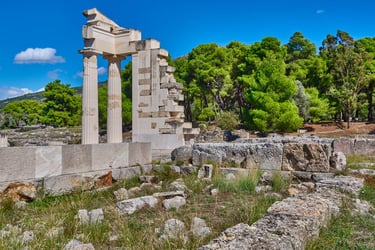 Ancient ruins of the Sanctuary of Asclepius at Epidaurus with stone columns and lush green trees.