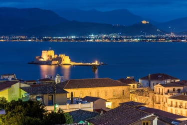 Illuminated Bourtzi Castle in Nafplio bay at night with city lights and mountains.