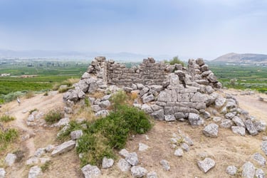 Ancient stone ruins of the Pyramid of Hellinikon overlooking a lush Greek valley landscape.