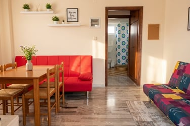 Modern living room with a red sofa, wooden dining table, and marble floor leading to a bathroom.