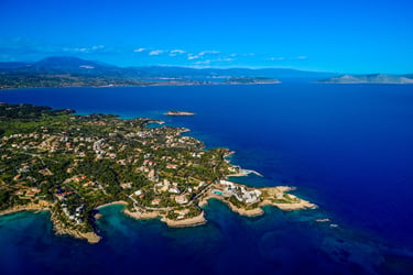 Aerial view of a coastal Greek town with luxury villas and turquoise Mediterranean sea water.
