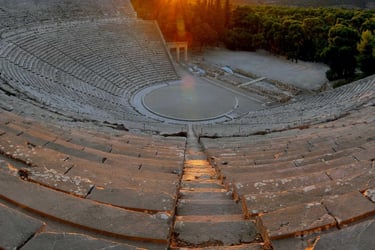 Golden sunset over the ancient Theater of Epidaurus in Greece with stone seating and mountains.