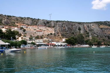 Scenic coastal village in Greece with waterfront tavernas and boats on turquoise sea water.