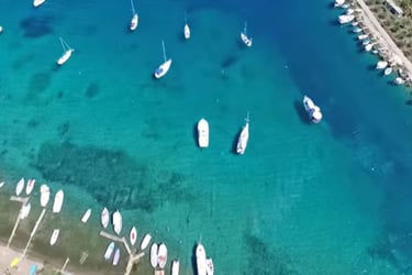 Aerial view of sailboats and motorboats anchored in a crystal clear turquoise bay along a tropical coastline.