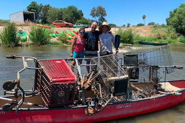 Group standing beside a kayak filled with trash and debris collected during a river cleanup.