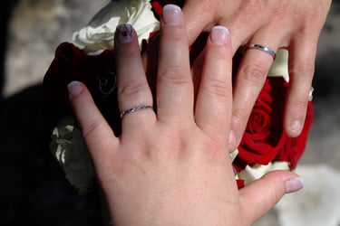 Mains des mariés avec leurs alliances sur fond de bouquet de fleurs